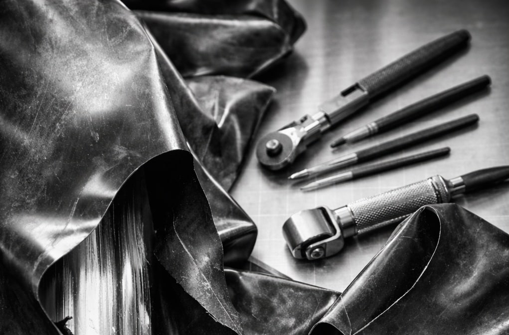 Detailaufnahme einer professionellen Latex Reparatur: beschädigtes schwarzes Latex auf einer Werkbank mit Reparaturwerkzeugen und sorgfältig ausgeführter Naht.